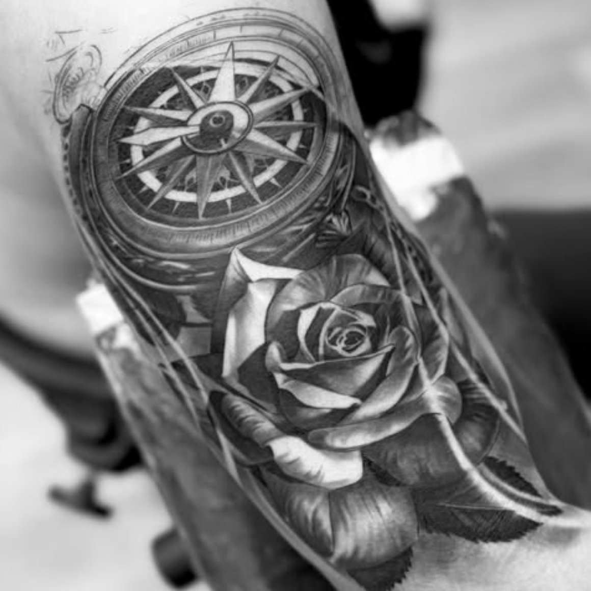 Black and white tattoo of a rose and compass on a person's arm.