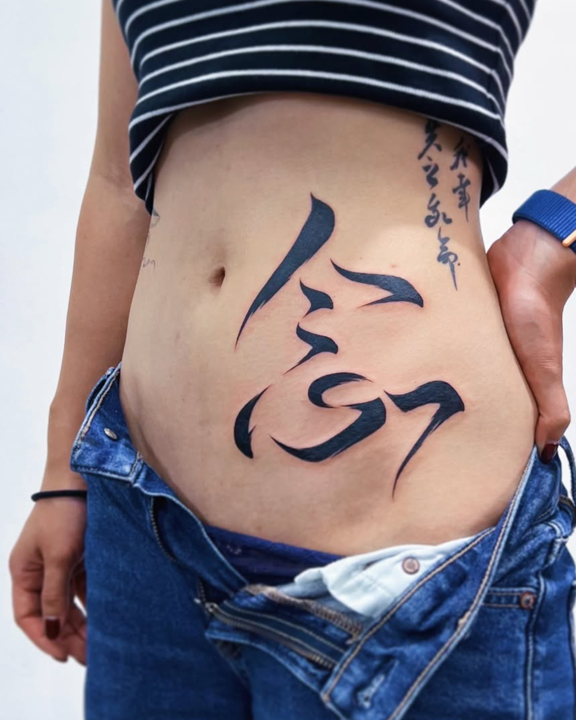 Person with black calligraphy tattoo on their stomach against a white background