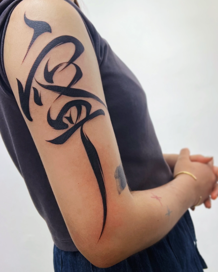 Person wearing a dark garment with a large black tattoo on their arm against a white background