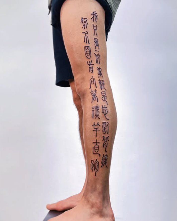 Person's leg with Chinese characters tattooed on a plain background