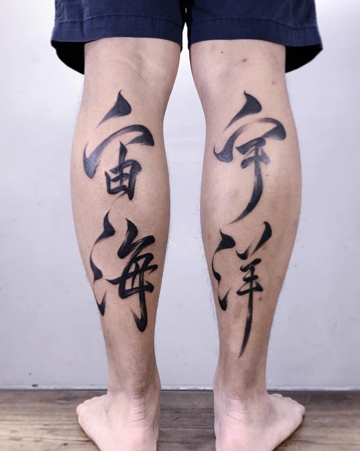 Person wearing dark shorts with black kanji tattoos on their legs against a plain background